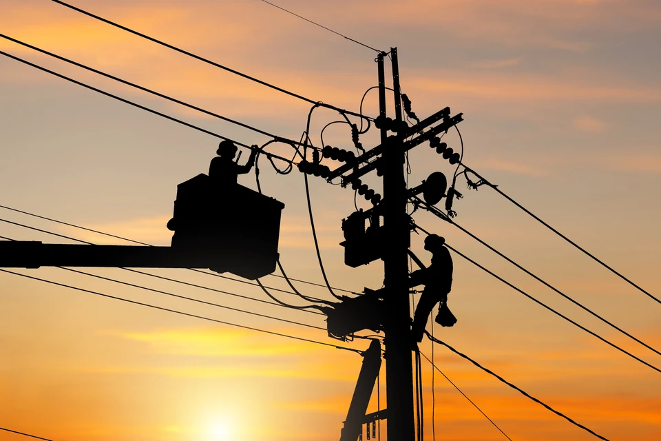 Scène extérieure au coucher du soleil avec technicien en silhouette travaillant sur poteau électrique