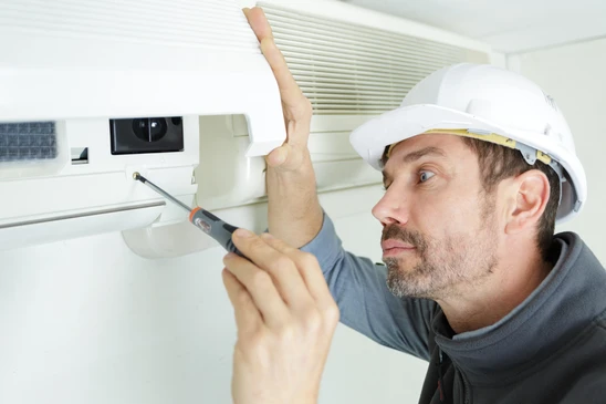 Un technicien en casque de sécurité blanc installe ou répare un système de ventilation au plafond d'un intérieur moderne