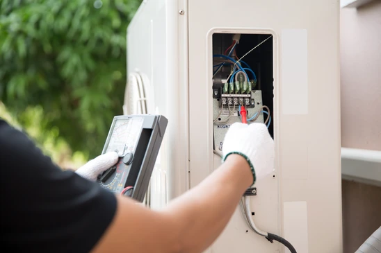 Technicien électricien en intervention extérieure utilisant un multimètre pour diagnostiquer un tableau électrique ouvert