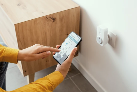 Femme mettant en place une prise intelligente à la maison en utilisant son smartphone, sa maison intelligente et son concept de domotique